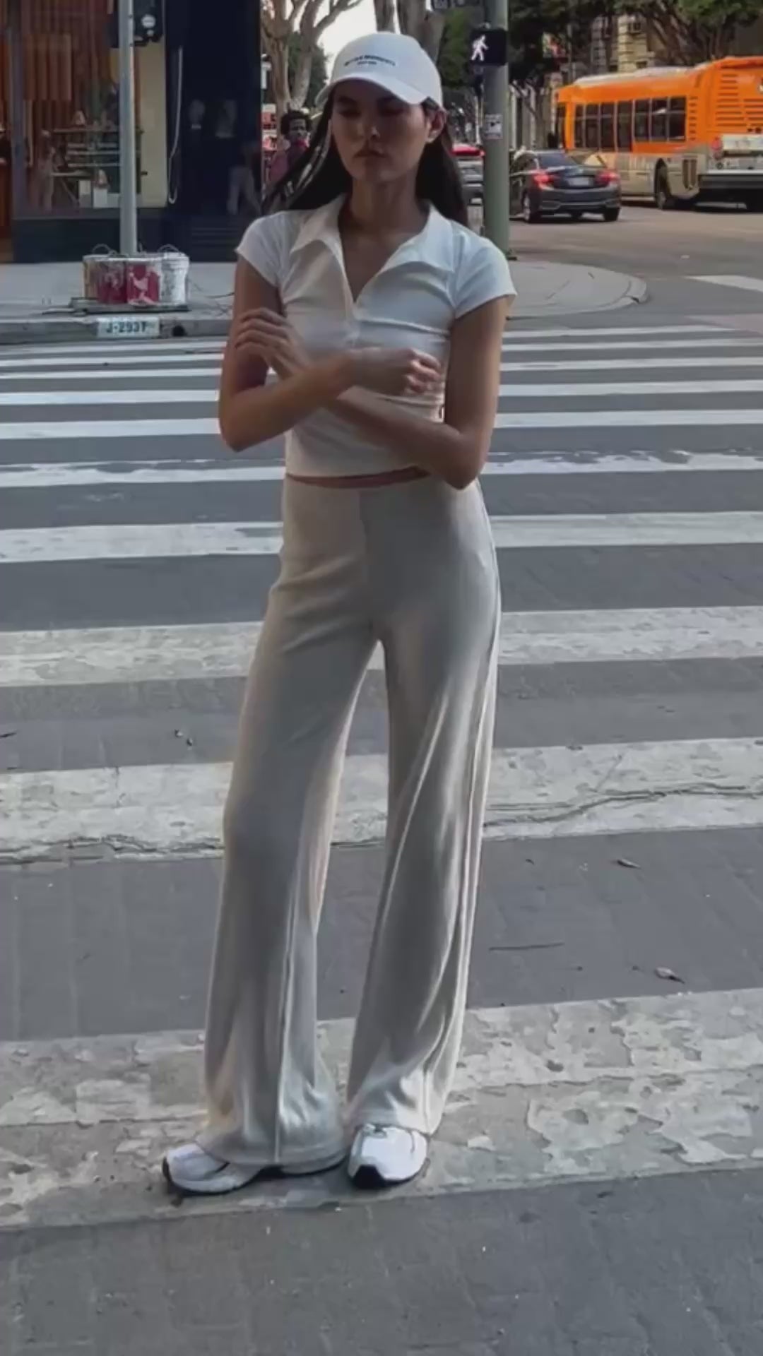 Model posing outdoors wearing BTTRMMT Rae Wide Rib Pant in light beige, styled with a fitted white collared top and white cap.